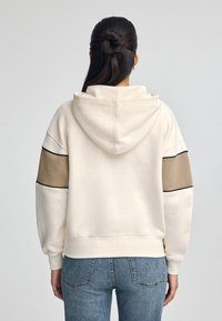 Felpa con cappuccio color avorio con accenti in blocco di colore beige e piping nero. Presenta una vestibilità rilassata e polsini a costine.