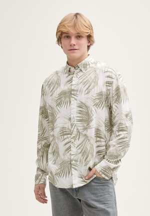Chemise à manches longues blanche avec un motif de feuille de palmier verte, un col boutonné et une coupe décontractée. Associée à un jean bleu clair.