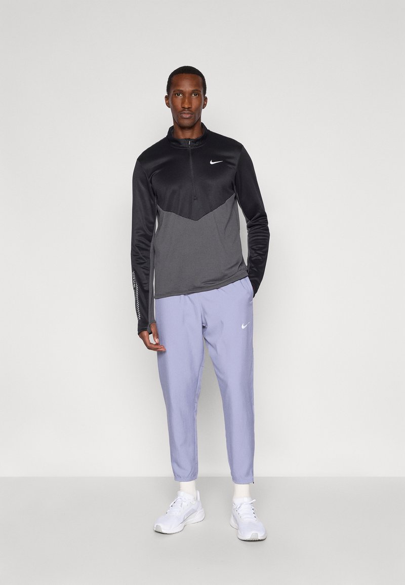 Sort og grå Nike langærmet træningstrøje med kvart lynlås, parret med lyse lilla tætsiddende bukser og hvide sneakers.