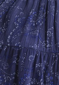 Mörkblått tyg med ett blommönster i ljusare blå nyanser. Det texturerade materialet har veck och delikata mönster genom hela.