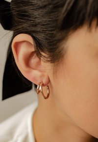 Se presentan aros de oro rosado, mostrando un acabado suave y brillante y un diseño circular clásico, colocados elegantemente en una oreja.