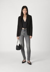 Svart tettsittende blazer, dyp V-hals topp, grå smale jeans, svart håndveske med kjede-reim, og svarte spisse leiligheter.