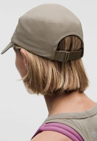 Beżowa czapka z teksturowaną powierzchnią, zakrzywionym daszkiem i regulowanym paskiem z tyłu, w zestawie z szaro-różowym topem na ramiączkach.