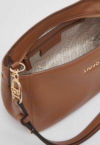 Sac à main en cuir marron avec une finition texturée, des ferrures dorées et une doublure intérieure à motif. Il dispose d'une fermeture éclair et d'une bandoulière.