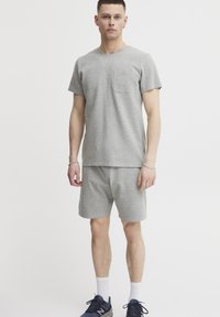Graues Baumwoll-T-Shirt mit kurzen Ärmeln und einer Brusttasche, kombiniert mit passenden grauen Shorts. Das Outfit hat eine lockere Passform und eine glatte Textur.
