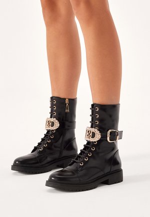 Black leather combat boots with lace-up front, gold-tone hardware, decorative buckle, and textured sole for grip.