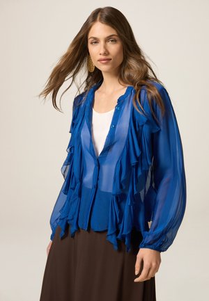 Hemdbluse in Blau mit transparentem Stoff, Rüschenschichten, durchgängigem Knopfverschluss und langen Ärmeln, kombiniert mit einem braunen Rock. Glatte Textur und fließendes Design.
