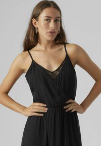 Robe noire avec un décollet é en V, des détails en dentelle au niveau de la poitrine, des épaules fines réglables et un tissu plissé fluide. Accentuée par une taille cintrée.