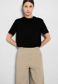 Juoda trumpa rankovė t-shirt su apvalia iškirpte, derinama su šviesiai ruda aukšto juosmens kelnėmis. Paprastas, minkštas audinys, laisvas siluetas.