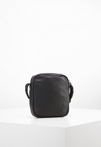 Svart läder crossbody-väska med rektangulär form, flätad handtag och dragkedjestängning. Slät yta utan ytterligare dekorationer.