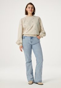 Lichtbeige pullover met bloemenborduursel in roze en bordeaux. Wijde mouwen en een aansluitende taille, gecombineerd met lichtgewassen flared jeans.