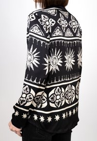 Schwarzes Langarmshirt mit weißen floralen und geometrischen Mustern, das eine glatte Stofftextur und einen geschwungenen Saum aufweist.