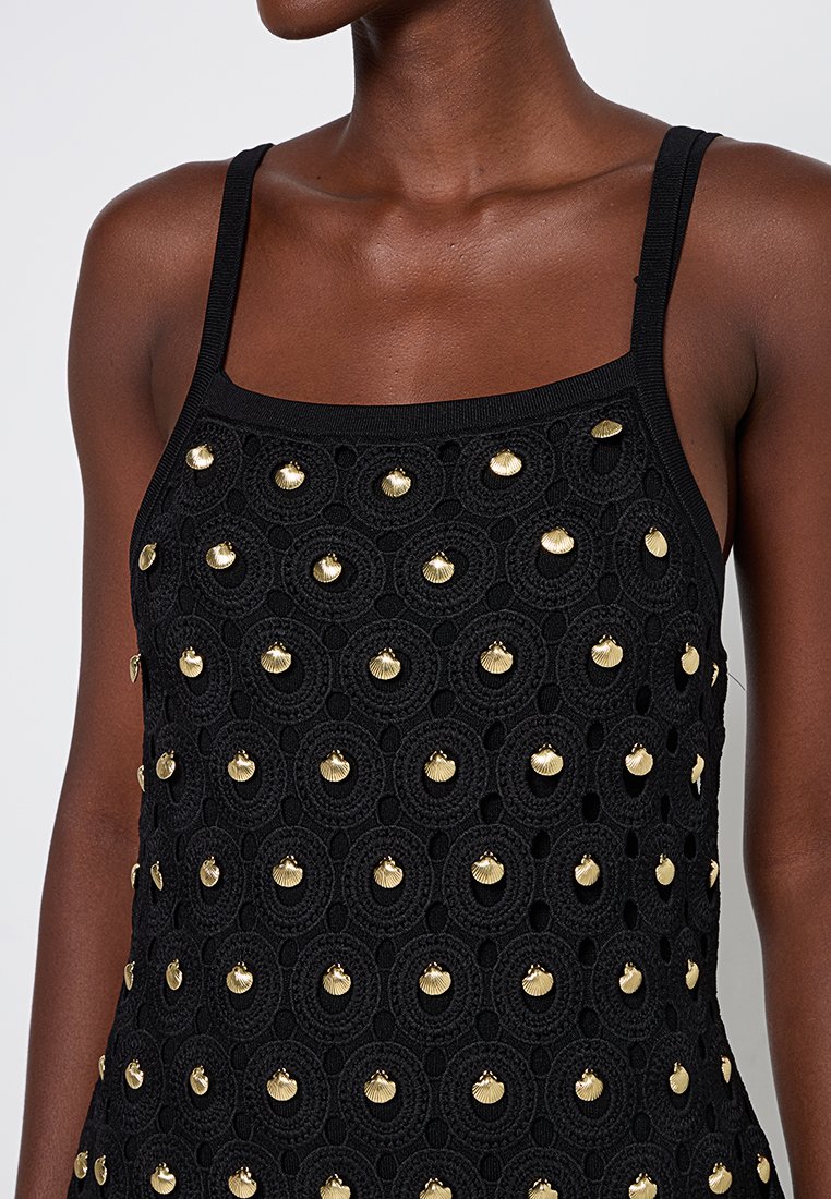 Schwarzes Top mit strukturiertem Design und runden Ausschnitten. Goldene, schalenförmige Verzierungen sind gleichmäßig verteilt. Verstellbare Träger.