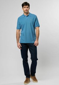 Világoskék póló, galléros nyakkal, sötétkék farmerral és barna sneakers-szel párosítva. Rövid ujjú, minimális márkajelzéssel rendelkezik.