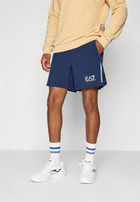 Navy blue athletic shorts with side pockets, featuring a white logo and gray accents, made of lightweight material for comfort.