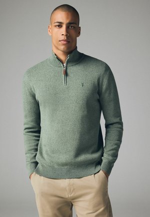 Grüner Pullover mit Reißverschluss und strukturiertem Strick, ausgestattet mit einem gerippten Saum und Bündchen. Das Design umfasst ein kleines Logo auf der Brust.
