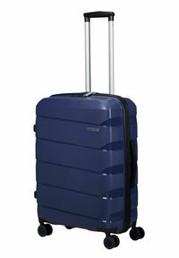 Spinner suitcase in navy blue hard shell, textured surface, vertical grooves, retractable handle, four wheels for mobility.