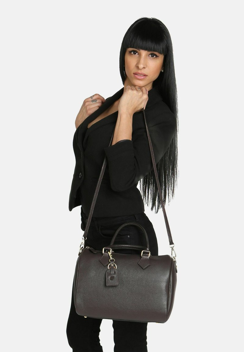 Borsa a mano in pelle marrone con texture liscia, forma arrotondata, doppio manico, tracolla rimovibile e dettaglio decorativo a chiusura.