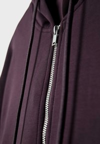Ljubičasti zip-up dukserica sa srebrnim patentnim zatvaračem, teksturirana tkanina i model koji se lepo prilagođava telu. Uključuje kapuljaču i glatke šavove za dodatnu izdržljivost.