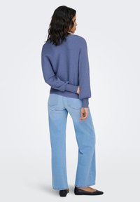 Pull-over en maille côtelée bleu, coupe décontractée avec manches longues. Associé à un jean large bleu clair et des ballerines noires.