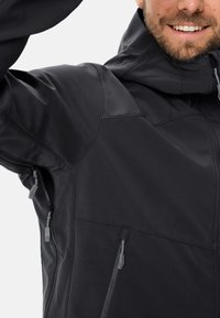 Giacca softshell nera con colletto alto, cappuccio regolabile e tasche con cerniera. Texture liscia e design ergonomico con dettagli cuciti.