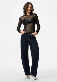 Crna bluzica s dugim rukavima posuta šljokicama kombinirana s tamnoplavim širokim trapericama i srebrnim cipelama s uskim vrhom. Upadljiva prozirna tekstura tkanine.