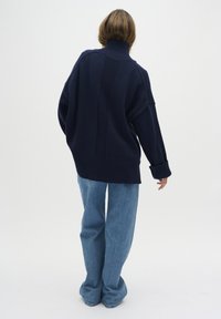 Marinblå överdimensionerad stickad tröja med hög krage, ribbade muddar och nederkant. Kombinerad med ljusblå vida denimjeans.