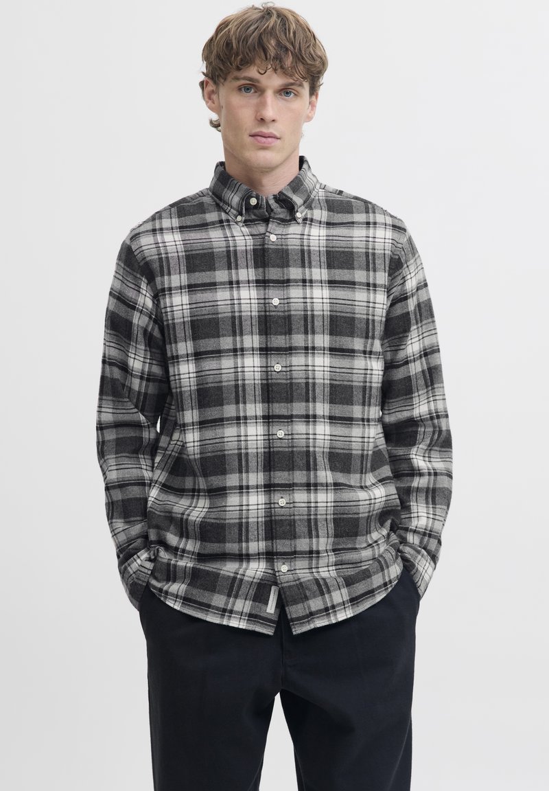 Rutete skjorte med knapper foran i svart og hvitt. Laget av mykt stoff med lange ermer og avrundet kant. Har krage og knapper foran.