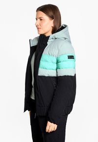 Color-blocked jacket featuring a mint green and black design, padded texture, zipper closure, and a hood. Material appears water-resistant.