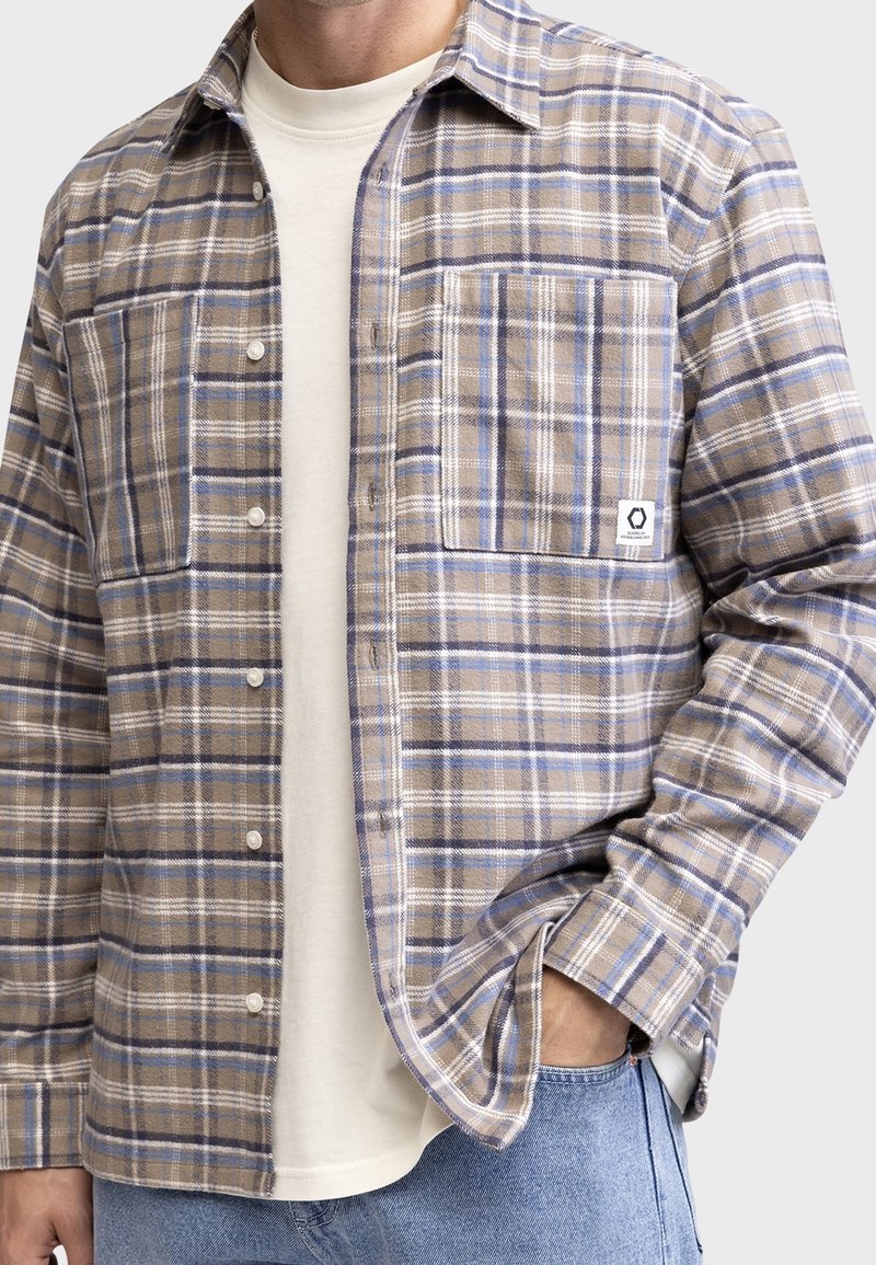 Kostkovaná košile v béžových a modrých tónech, vyrobená z flanelu. Má zapínání na knoflíky, dvě náprsní kapsy a tkanou nálepku na levé kapse.
