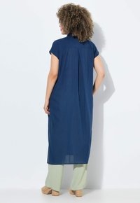 Granatowa sukienka do kolan z krótkimi rękawami, kołnierzykiem i plisą z tyłu. Połączona z jasnoskalnymi szerokimi spodniami i koturnami.