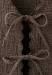 Gros plan d'un tissu texturé brun foncé avec des bords festonnés, noué avec deux nœuds en tissu doux assortis.