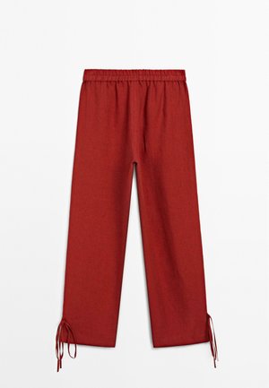 Red, loose-fitting pants with an elastic waistband and drawstring at the cuffs, made of textured fabric. Flat, straight leg design.