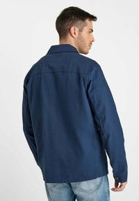 Marineblauwe jas met een comfortabele pasvorm, knoopmanchetten en een klassieke kraag. Gemaakt van structuurstof, met een rechte snit en een rugnaad.