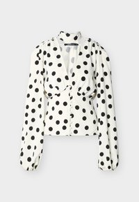 Λευκό πουκάμισο με μαύρες πουά βούλες, μακριά φουσκωτά μανίκια, βαθύ V-λαιμόκοψη και κουμπιά καλυμμένα με ύφασμα κατά μήκος του μπροστινού μέρους.