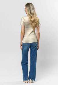 Svītraina smilšu krāsas un baltas krāsas pielāgota T-kreklā, apvienota ar zilu platu kāju džinsu un gaišām kurpēm. Mati maigi viļņojoties krīt uz muguras.