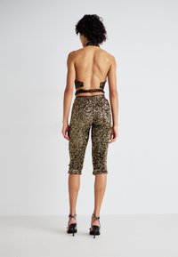 Vue de dos d'une personne portant un haut sans dos à motifs métalliques et un pantalon court en sequins dorés, rehaussé d'un détail en forme d'anneau doré.