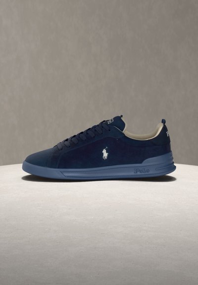 Ναυτικό μπλε sneaker Polo με λευκό λογότυπο στο πλάι, μπλε σόλα, σχέδιο με κορδόνια και μαξιλαρωμένο κολάρο, εμφανίζεται από τη δεξιά πλευρά σε ουδέτερο φόντο.