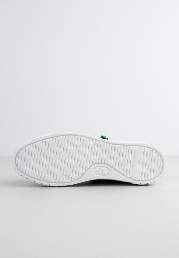 Weiße Gummisohle mit strukturiertem Grip, die eine leichte Kurve und einen grünen Akzent in der Nähe der Ferse aufweist. Das Design ist schlicht und funktional.