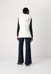 Vitt vadderat väst med huva, med quiltade sektioner. I kombination med mörkblå utsvängda jeans och svart topp. Skor med klackar som når smalbenen synliga.