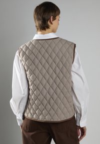 Quilted vest i brun og creme tartanmønster, med rund hals og ærmeløs design. Kan sættes sammen med en hvid skjorte under.
