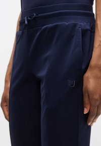 Μπλε ναυτικό αθλητικό παντελόνι με ελαστική ζώνη μέσης με κορδόνι, ομαλή υφή, με διακριτικό λογότυπο στο πλάι για τη διάκριση της μάρκας.