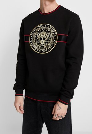 Zwarte sweatshirt met gouden lion borduursel in het midden, rode accentstrepen op de schouders en onderrand, geribbelde mouwen en kraagdetails.