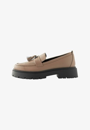 Beige Lederloafers mit Quastenakzent, ausgestattet mit einer klobigen schwarzen Plateausohle und strukturiertem Obermaterial, entworfen für Komfort und Stabilität.