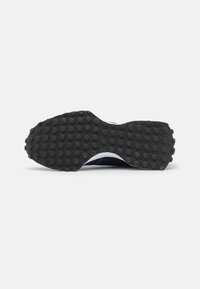 Semelle de chaussure en caoutchouc noire avec des grips ronds texturés, présentant une légère courbure ascendante au niveau des orteils et un bord lisse et structuré.