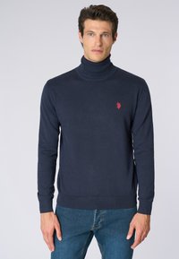 Maglione a collo alto in maglia navy con orlo e polsini a costine, decorato con un piccolo logo rosso sul lato sinistro del petto. Tessuto morbido, design aderente.
