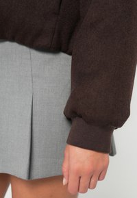 Brązowy sweter o teksturowanej tkaninie i prążkowanych mankietach, w połączeniu z plisowaną szaro-skalną spódnicą, o gładkiej tkaninie i dopasowanym kroju.