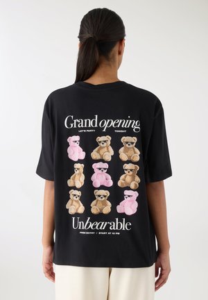 Maglietta nera oversize con orsetti multicolori stampati sul retro, con testo che recita "Grande apertura" e "Insopportabile."