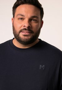 Camiseta azul marino de cuello redondo, hecha de una tela suave. Presenta un sutil logo negro en el pecho y un diseño minimalista.