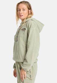 Fleece-Hoodie in hellgrün mit gesticktem Logo und gemustertem Saum. Verfügt über eine Fronttasche und eine Kapuze mit Kordelzug.